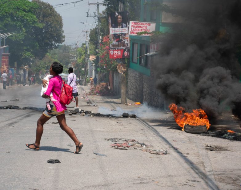 Uma mulher carregando uma criança corre da área após tiros serem ouvidos em Porto Príncipe, Haiti, em 20 de março de 2024.(Clarens Siffroy / AFP via Getty Images)