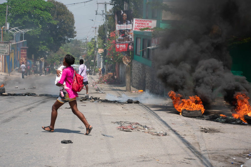 Uma mulher carregando uma criança corre da área após tiros serem ouvidos em Porto Príncipe, Haiti, em 20 de março de 2024.(Clarens Siffroy / AFP via Getty Images)