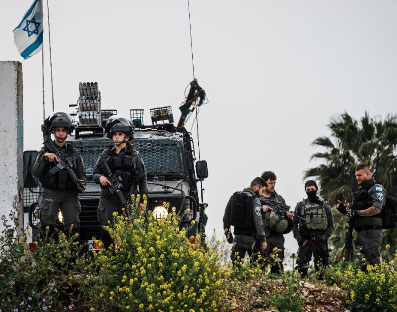 Soldados israelenses monitoram moradores palestinos da Cisjordânia com autorizações condicionais que cruzavam um posto de controle para entrar em Jerusalém e rezar na Mesquita de Al-Aqsa durante o Ramadã, em Qalandia, na Cisjordânia ocupada, na sexta-feira, 29 de março de 2024. (Marcus Yam / Los Angeles Times)